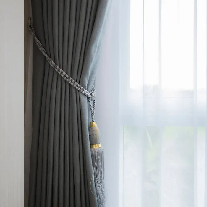 Grey curtain held by a tieback beside a sheer layer